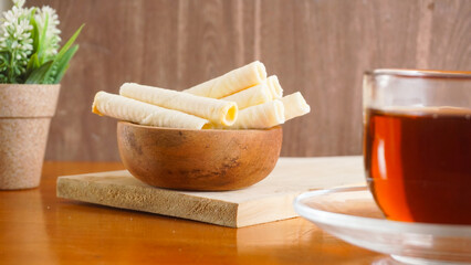 Delicious wafer rolls snack with sweet cheese cream filling serving on plate with a cup of tea...