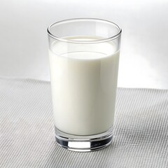 A clear glass filled with fresh white milk sitting on a textured white surface in a well lit setting