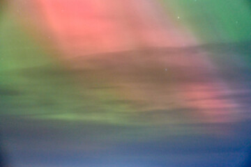 Bright purple green pink blue northern lights in night sky casting vibrant hues over dark landscape...