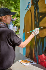 Young adult female artist with gloves and cap painting vibrant mural. Focused, intent expression....