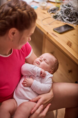 Young female with braided hair, wearing pink shirt, cradles infant girl in relaxed, cozy home environment. Muted lighting enhances serene moment