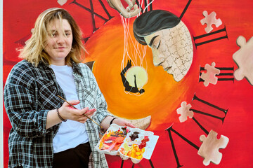 Young woman holding paint palette stands by vibrant surreal clock painting with puzzle patterns....
