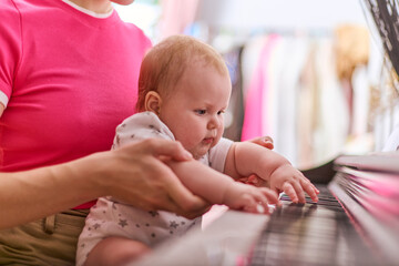 Young woman guides baby girl on synthesizer keys. Bright room, casual setting. Baby focused,...
