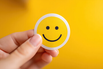 Hand holding happy smiley face sticker on bright yellow background top view