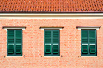 Fototapeta premium Three dark green shutters on a light brick building with a terracotta roof; sunny, Mediterranean style.