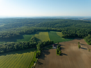 Aerial view of the landscape showing a mix of lush green forests, agricultural fields, and a small building, Zillisheim, Grand Est, France.