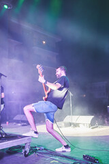 Fototapeta premium Male bassist performing energetically on stage during night concert