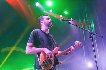 Obraz premium Bass guitarist singing on stage under colorful green and red concert lights