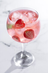 Strawberry gin tonic cocktail on white marble background.