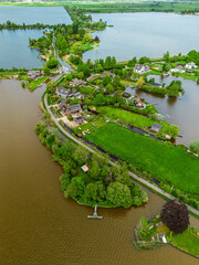 Aerial view of a scenic lakeside village with narrow peninsulas, green fields, and houses...