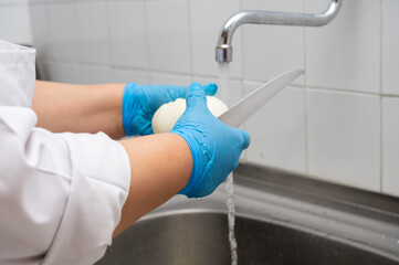women's hands clean onions with a knife under the tap with water in the sink at a commercial kitchen. High quality photo
