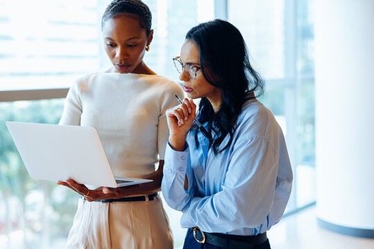 Two female professionals working together on a laptop in a bright office environment