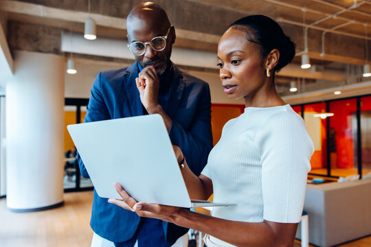 Two professionals discussing work details while looking at a laptop in an office - Powered by Adobe