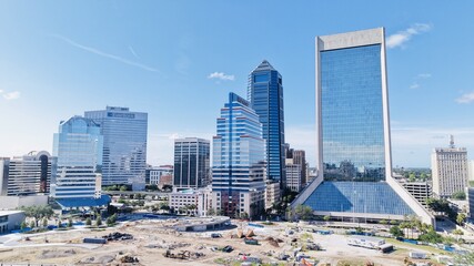 Aerial view of modern skyscrapers piercing the clear blue sky, juxtaposed with a construction site's raw earth tones, Jacksonville, Florida, United States.