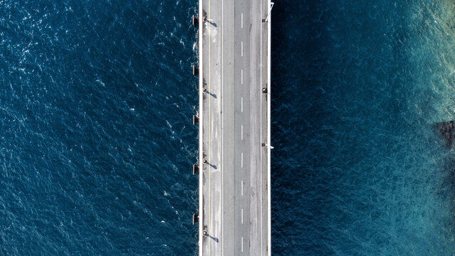 Aerial view of a road bridge cutting a stark grey line through the shimmering, turquoise waters of the Adriatic Sea, Split, Split-Dalmatia County, Croatia.