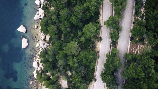 Aerial view of the rugged coastline kisses the Adriatic Sea, a lush forest meets a winding road, Split, Split-Dalmatia County, Croatia.