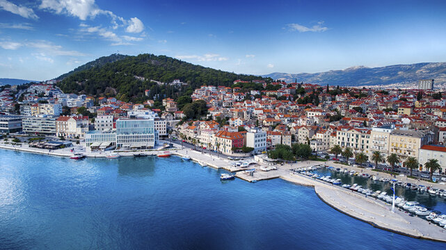 Aerial view of the azure Adriatic Sea meeting the red-roofed buildings of Split beneath the green Marjan hill, Split, Split-Dalmatia County, Croatia.