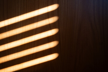 Sunlight streaks pattern projected on wooden wall by window roller shutters.