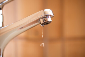 Dripping tap with water droplets inside apartment bathroom. Macro, close up shot, shallow depth of...