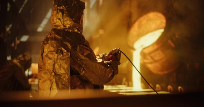 Furnace Operators in Protective Fireproof Suits and Industrial Employees Working at a Modern Metal Foundry. Foundrymen Pouring Hot Melted Iron Ore into Casting Forms, Producing Equipment
