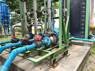 Water pump system with blue PVC piping and black storage tank in an outdoor industrial setting. Pressure gauges and motor pumps installed for fluid distribution and process efficiency.