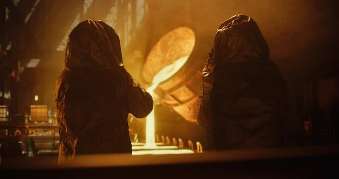 Team of Foundrymen in Reflective Suits Managing the Flow of Liquid Metal Inside an Industrial Smelting Facility. Precise Coordination Ensures Safe Pouring into Preheated Molds