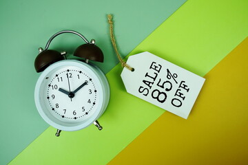 Sale 85% off text on price tag with alarm clock on green, yellow geometric background