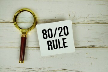 80/20 Rule text message on paper with magnifying glass on wooden background