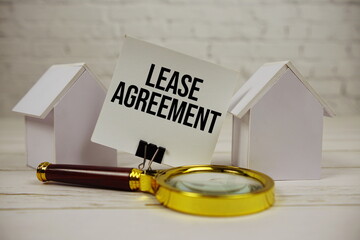 Lease Agreement text message on paper with magnifying glass and house model on wooden background