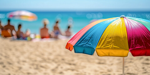 close up of a colorful beach umbrella with people relaxing by the sea on a summer day in background - summer vacation concept