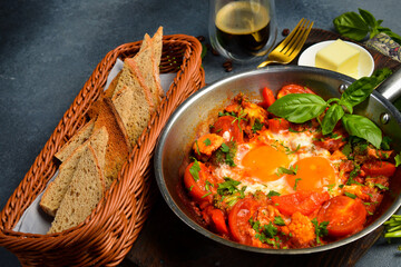 Shakshuka eggs in a pan with toast on a black concrete background. Poached eggs in a spicy tomato pepper sauce. Traditional Jewish breakfast. Healthy meal.