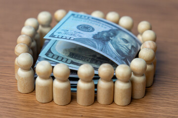 A stack of U.S. hundred-dollar bills surrounded by a wooden human figurines. Crowdfunding concept.