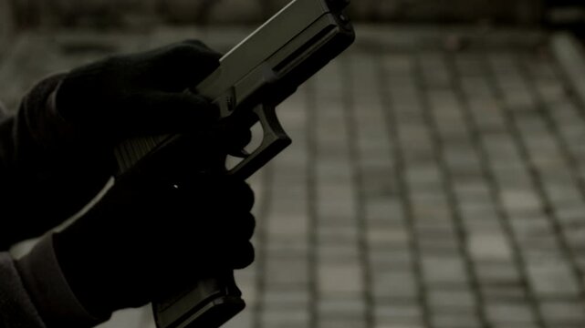 Black and white video hands of a man in gloves with a weapon or pistol reloading him. Bandit, criminal, thief, robber