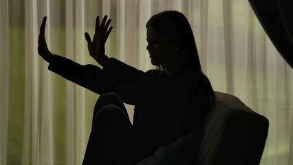 Silhouette of a woman sitting on a couch and showing a stop gesture.