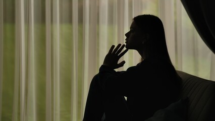 Silhouette of a distressed woman in front of backlit curtains