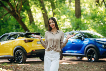 Choice between the blue or yellow ones. Young woman is in the forest with two cars