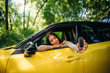 Happy owner is holding keys. Woman is with her car in the forest