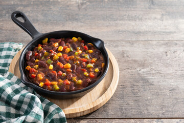 Mexican chilli beans with vegetables in iron pan on wooden table. Copy space