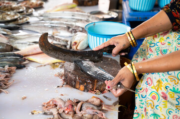 Indian woman cutting fish on a market in Mumbai India, sales stall with freshly caught seafood,...