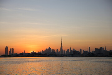 Naklejka premium Sunset over Dubai skyline with Burj Khalifa reflected on water.