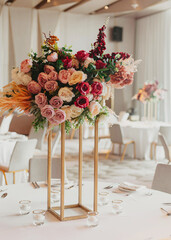 Tall floral centerpiece with roses and greenery on an elegant wedding reception table.
