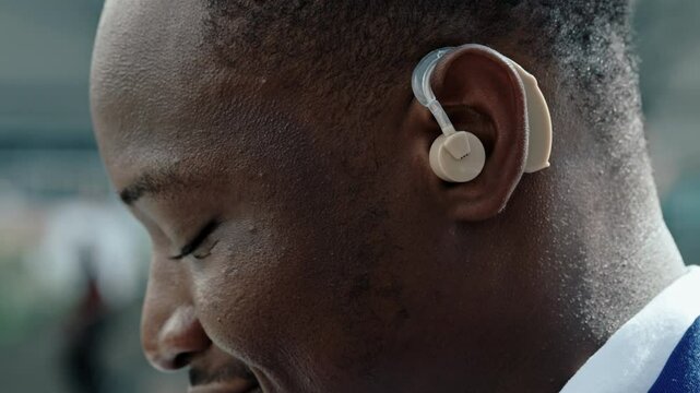 Portrait of cheerful African American office worker with hearing impairment stands outdoors. Young businessman with disability preforms inclusion in corporate workplace closeup
