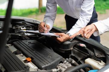 Insurance Assessment. A professional inspecting a car engine while discussing with a client.