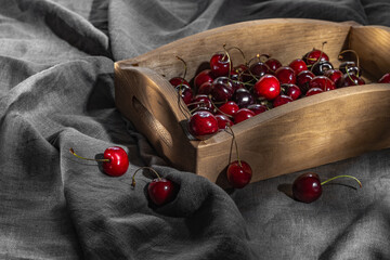 A wooden tray with ripe cherries on a gray tablecloth.