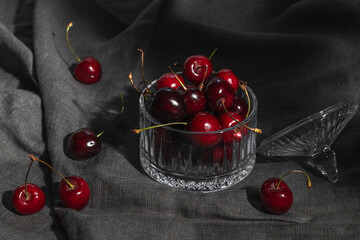 A glass vase with ripe red cherries on a gray tablecloth.