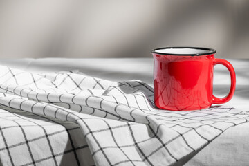 A red mug stands on a checkered napkin.