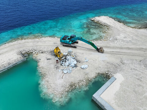 Aerial view of an excavator and breaker reshaping the coastline where turquoise waters meet white sands, Maalhos, Baa Atoll, Maldives.