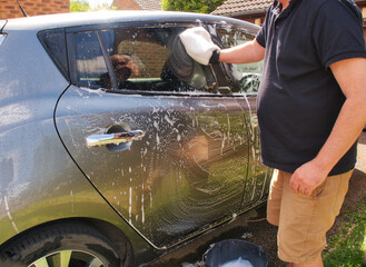 Close-Up of a man washing a silver car with a hand glove in a driveway at home