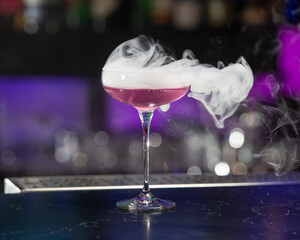 This visually striking pink alcoholic cocktail in a coupe glass features a large with more smoke...