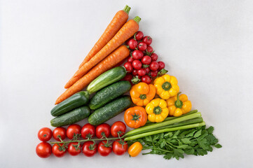 shows a variety of colorful vegetables arranged in a triangle shape on a light grey background. The vegetables include carrots, cucumbers, tomatoes, bell peppers, and celery, showcasing a rainbow of c